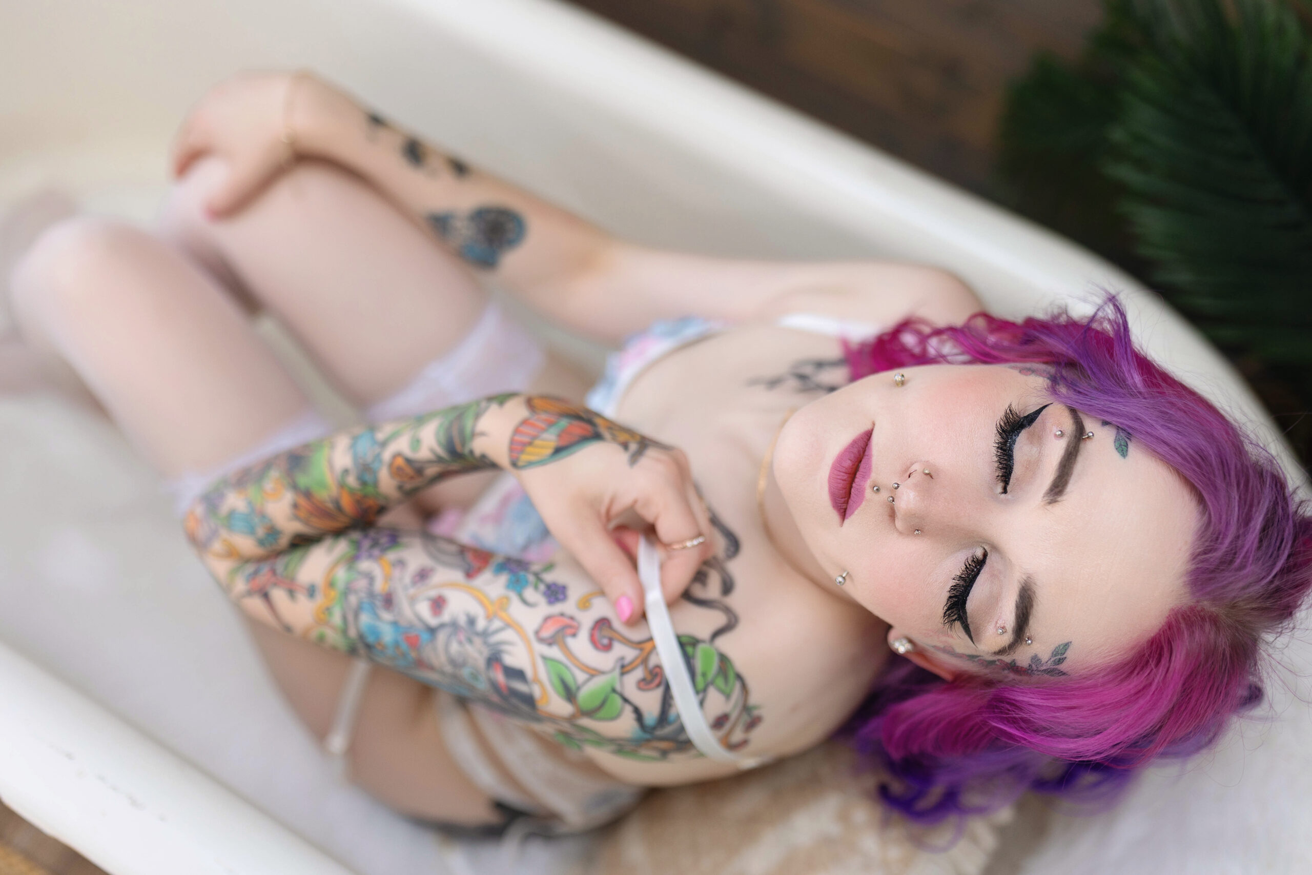 fair skinned women with coloerful hair and tattoos laying in a vintage tub for a sunroom boudoir session