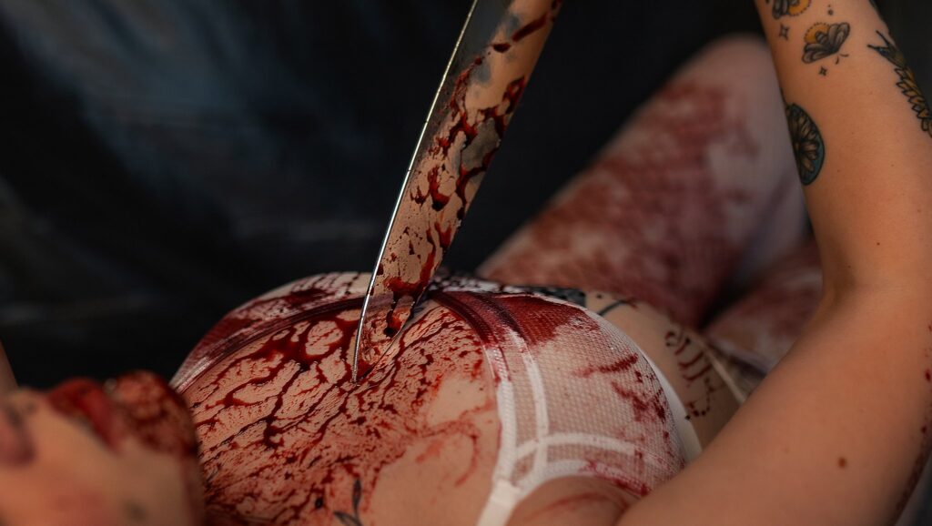 Knife covered in faux blood resting on Abigail’s chest during her Dexter-themed session.