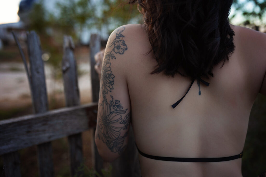  Close-up of Thalia’s floral tattoo against a rustic fence during her Western boudoir session.