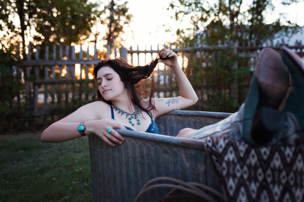 Thalia lounging in a vintage tub with turquoise jewelry, embracing a western boudoir style.
