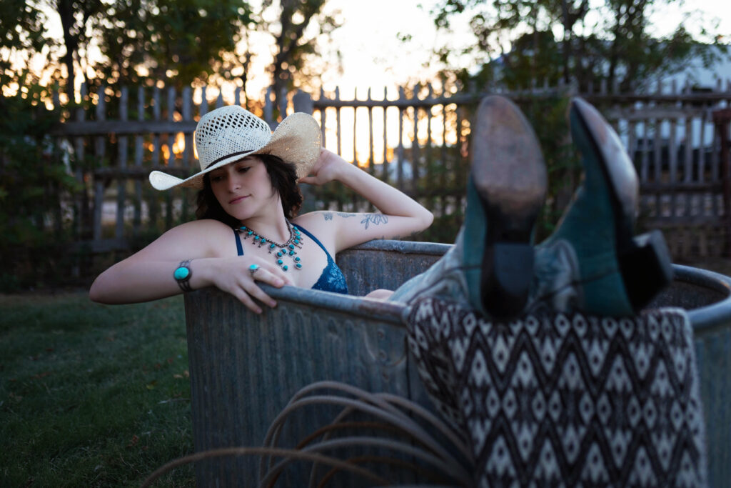 Thalia posing in a cowboy hat and turquoise accessories in a galvanized tub, capturing a Western boudoir vibe